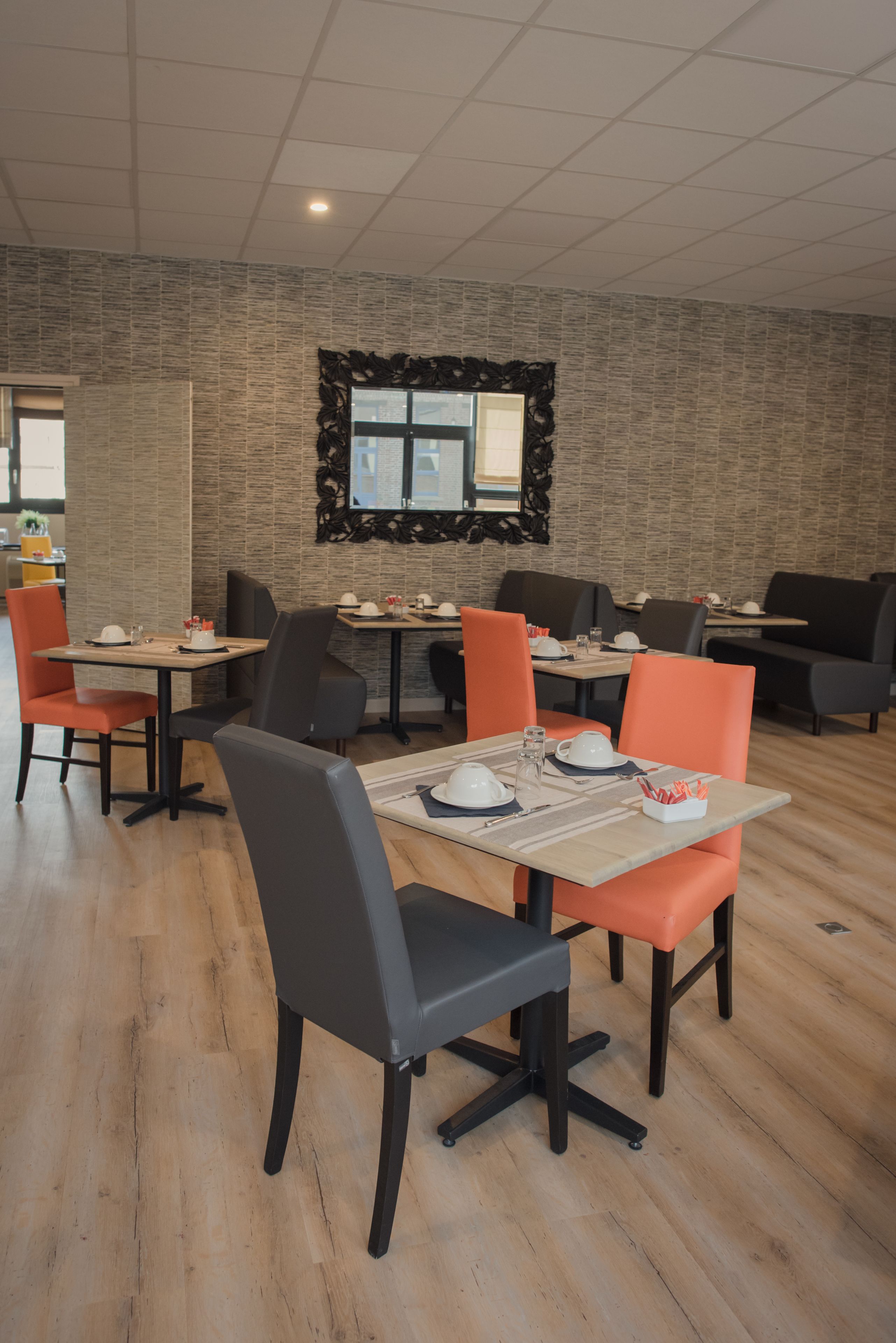 A modern dining area with multiple tables and chairs, featuring a brick wall and a large window.