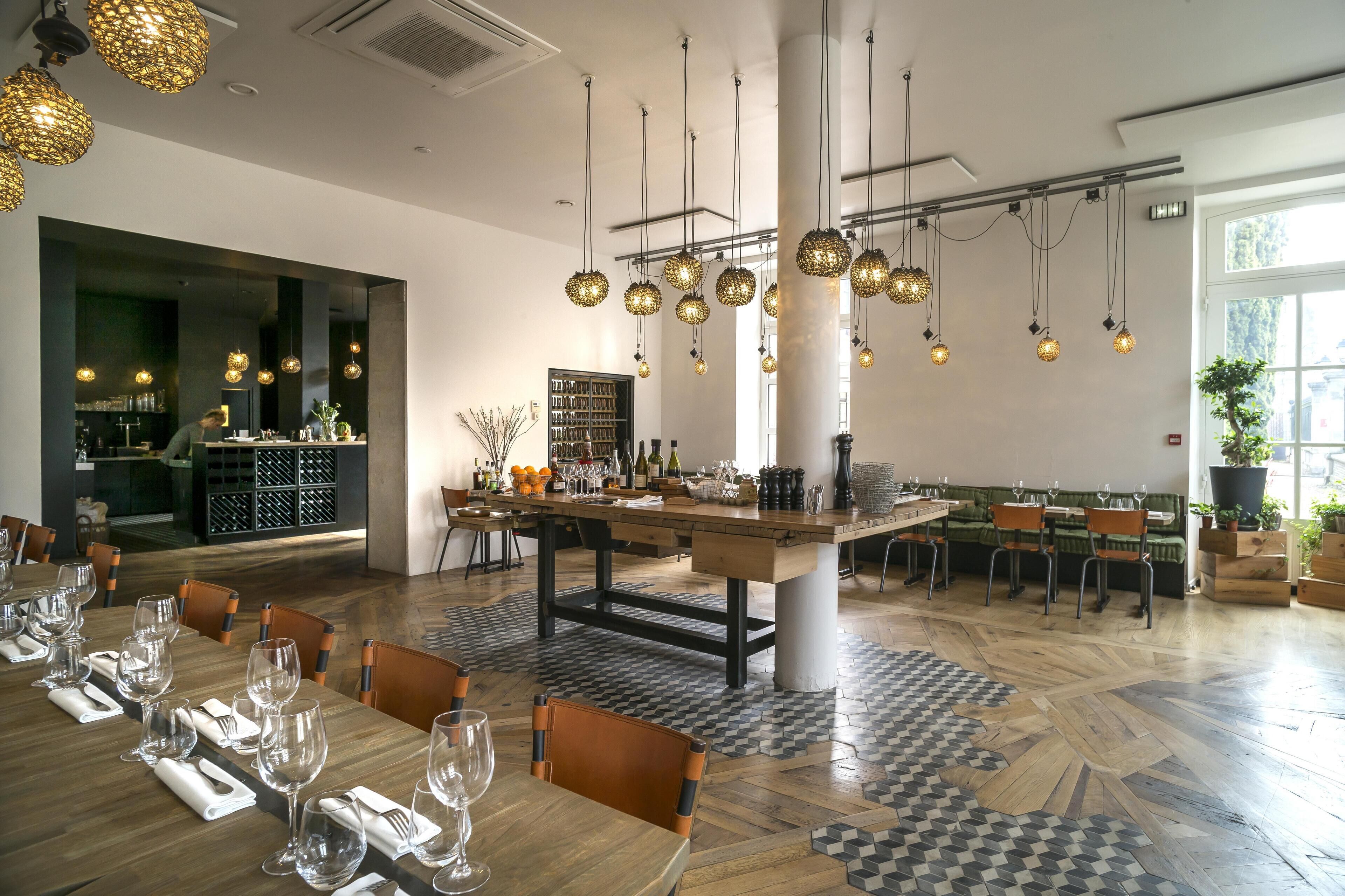 A restaurant with a long wooden table set for dining, hanging spherical light fixtures, and a checkered floor pattern.