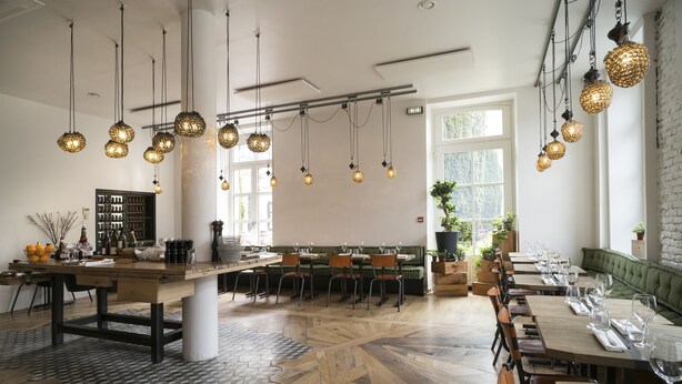 Ein Restaurant mit einem langen Holztisch, mehreren hängenden, kugelförmigen Leuchten und einem gemusterten Boden.