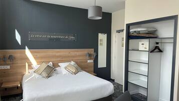 A modern hotel room with a large bed, bedside lamps, a wardrobe, and a quote on the wall.