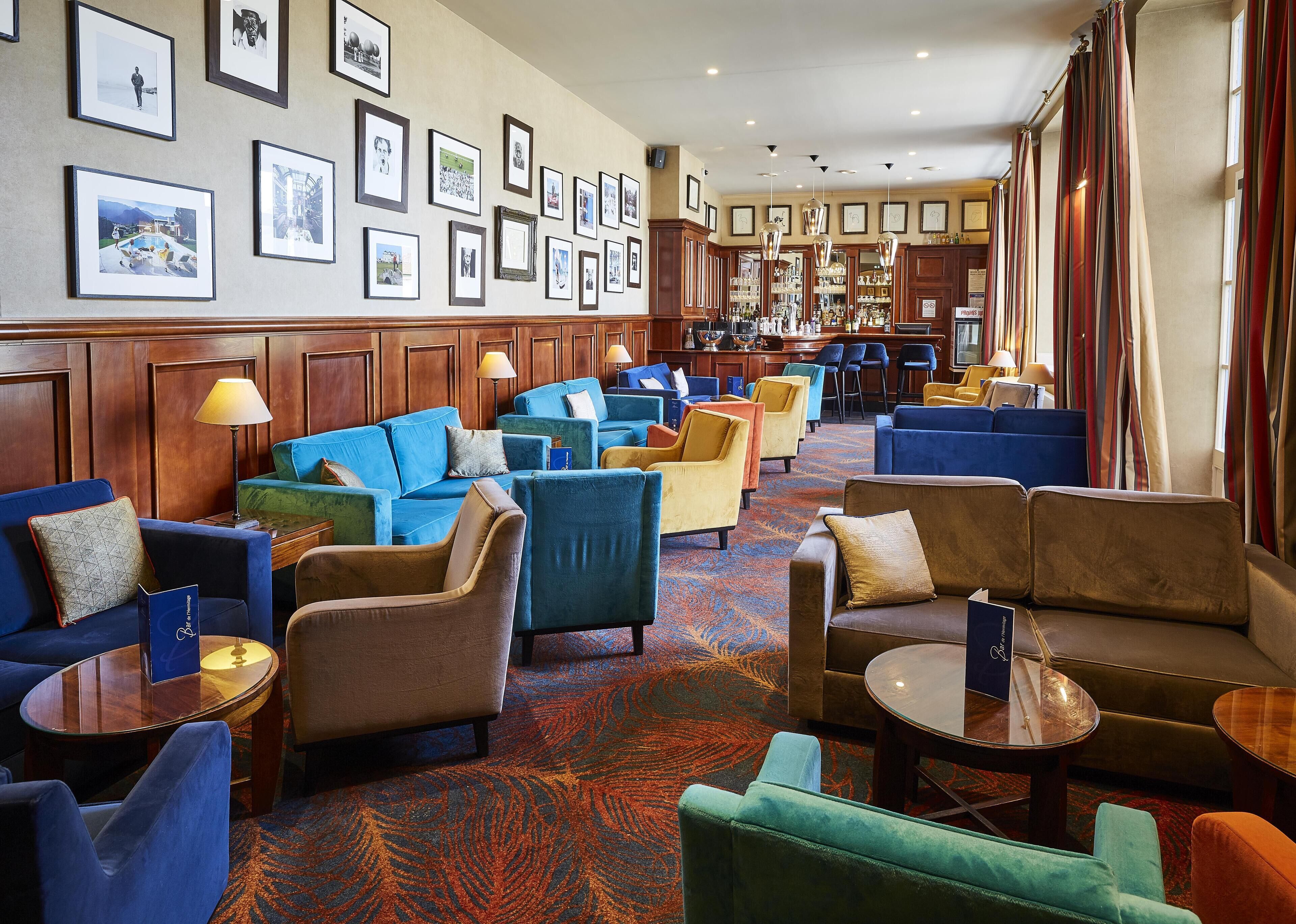 A hotel lobby with multiple seating areas, a bar, and framed pictures on the walls.