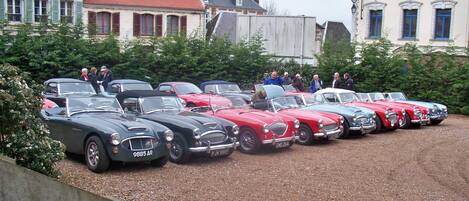 A row of vintage cars parked on a gravel surface with buildings in the background.