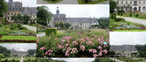 A historic building with a symmetrical garden layout, featuring neatly trimmed hedges and a variety of flowering plants.