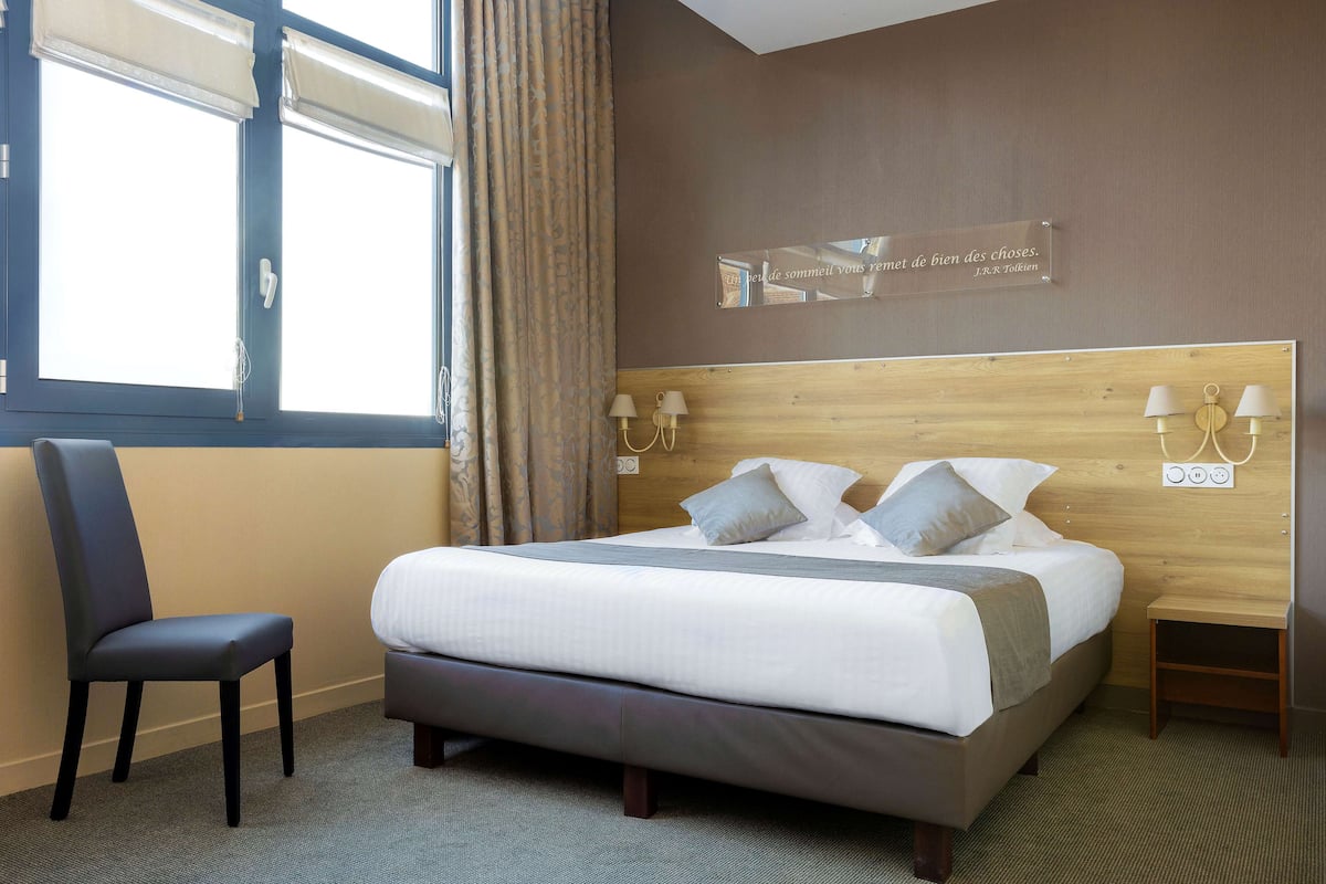 Una habitación de hotel ordenada con cama, una silla y una mesita de noche.