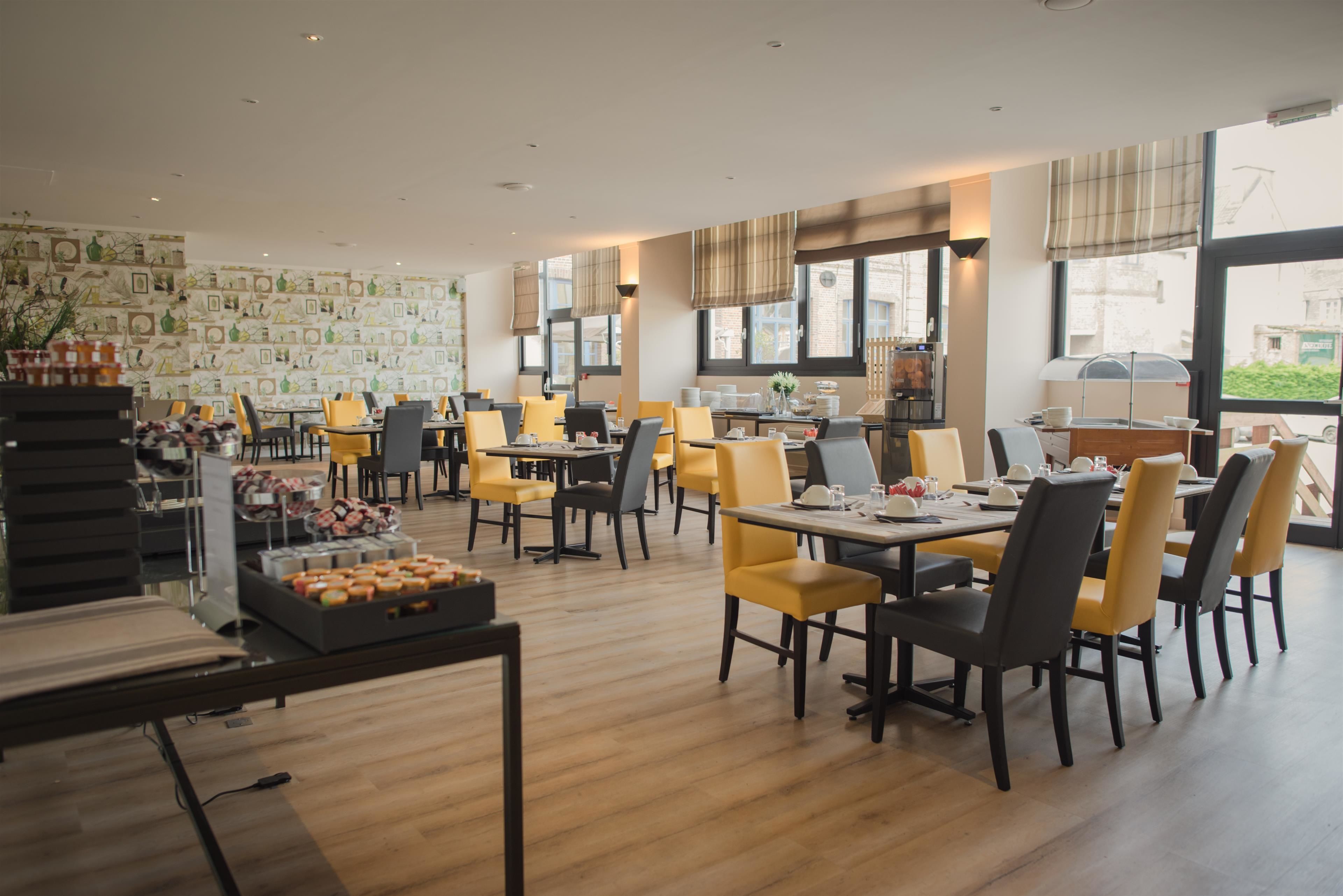 Un restaurant spacieux, doté de nombreuses tables et chaises, d’un plancher en bois et de grandes fenêtres offrant une vue sur l’extérieur.