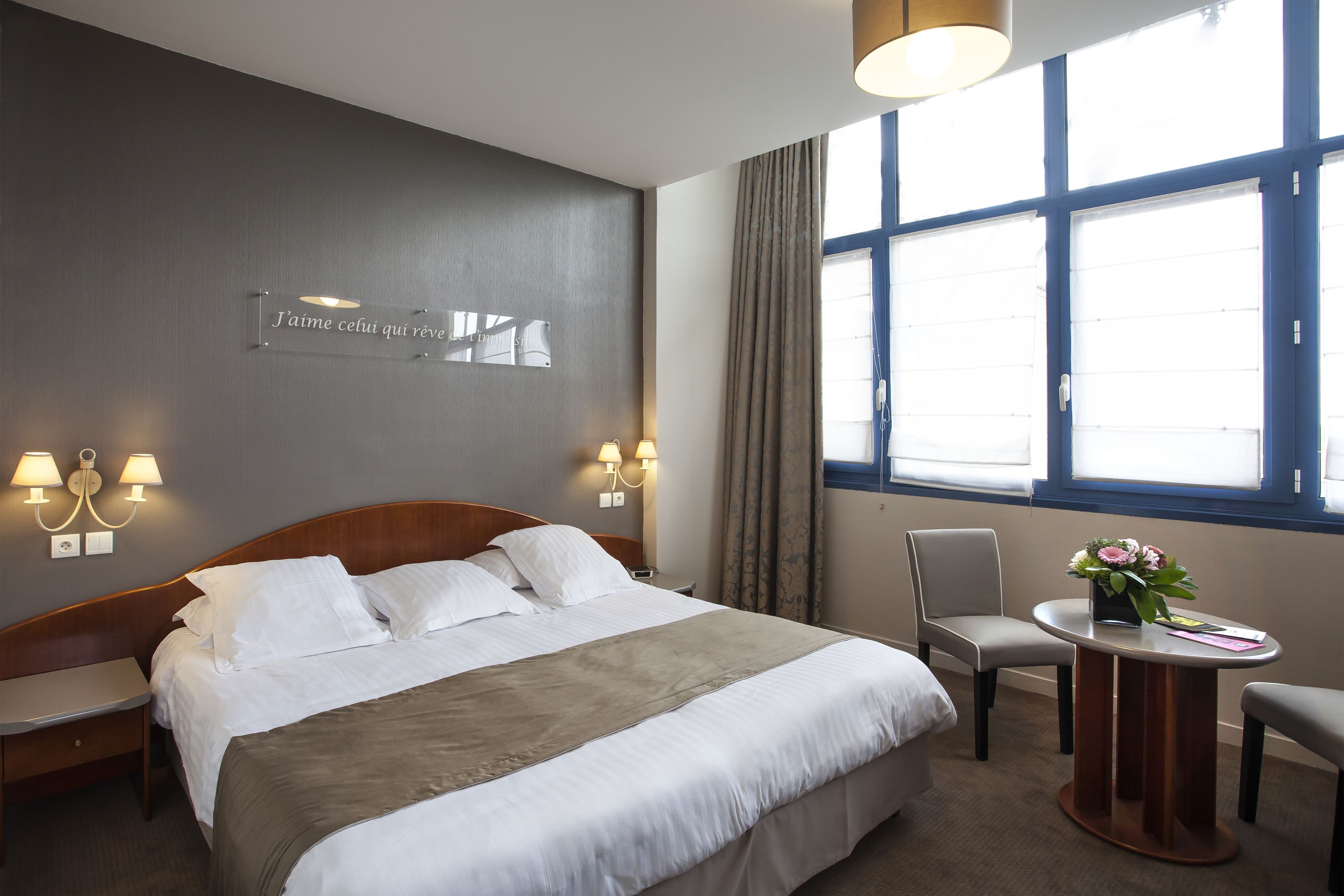 Une chambre d’hôtel avec un grand lit, des tables de chevet, un bureau, une chaise et une fenêtre avec des rideaux.