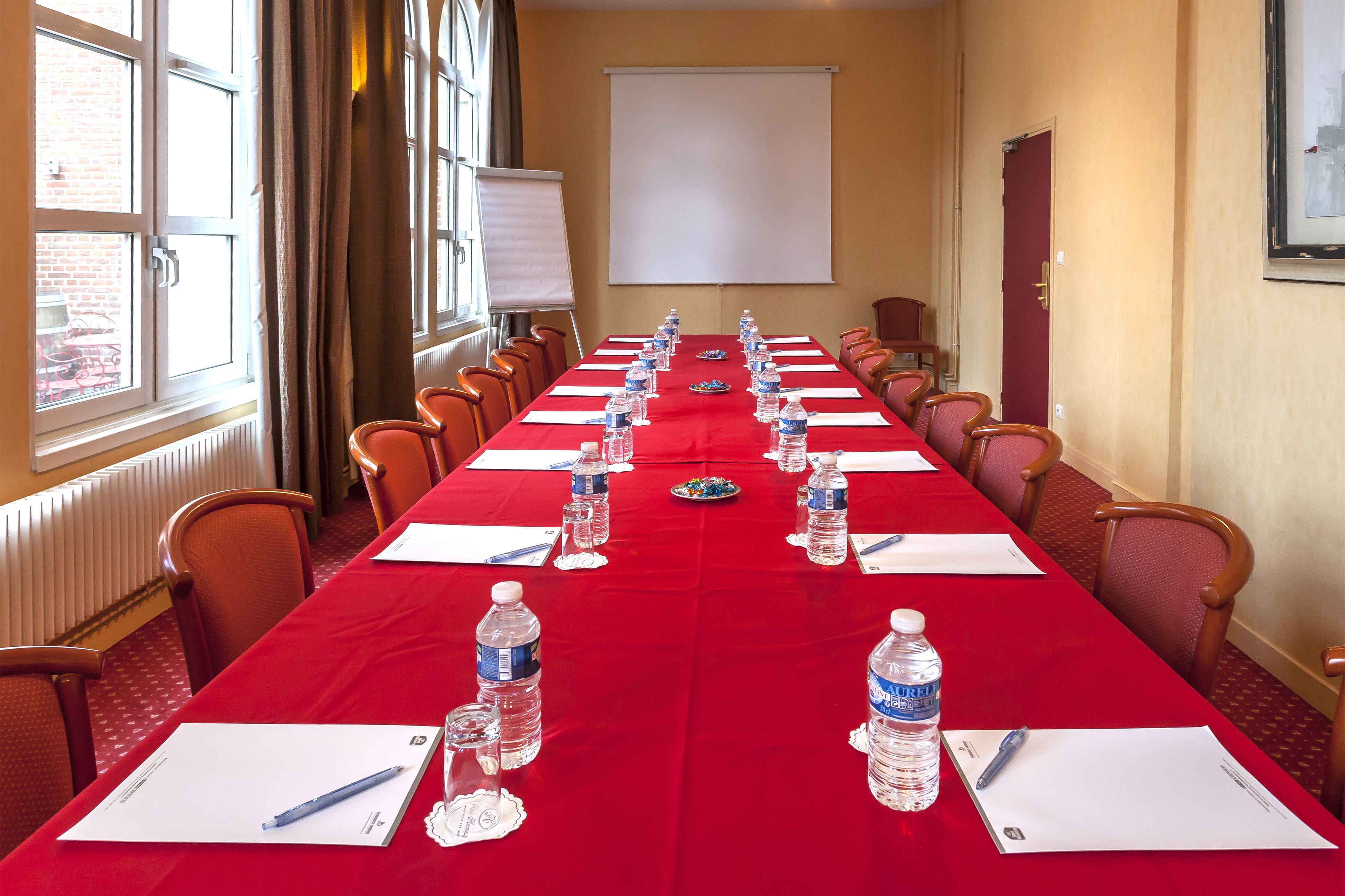 A conference room with a long table, chairs, water bottles, and a projector screen.