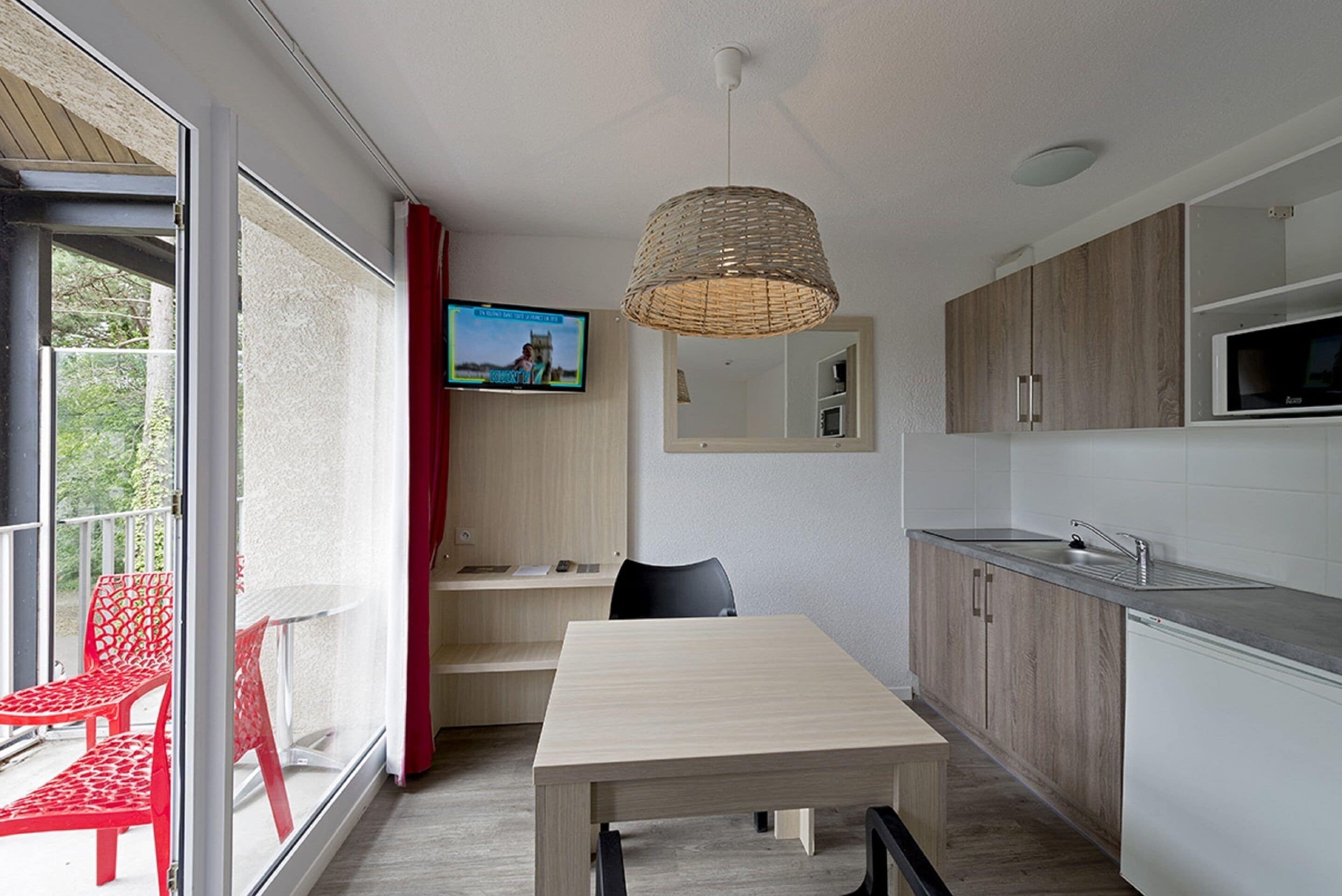 Een moderne keuken met een eethoek, een televisie en een balkon met rode stoelen.