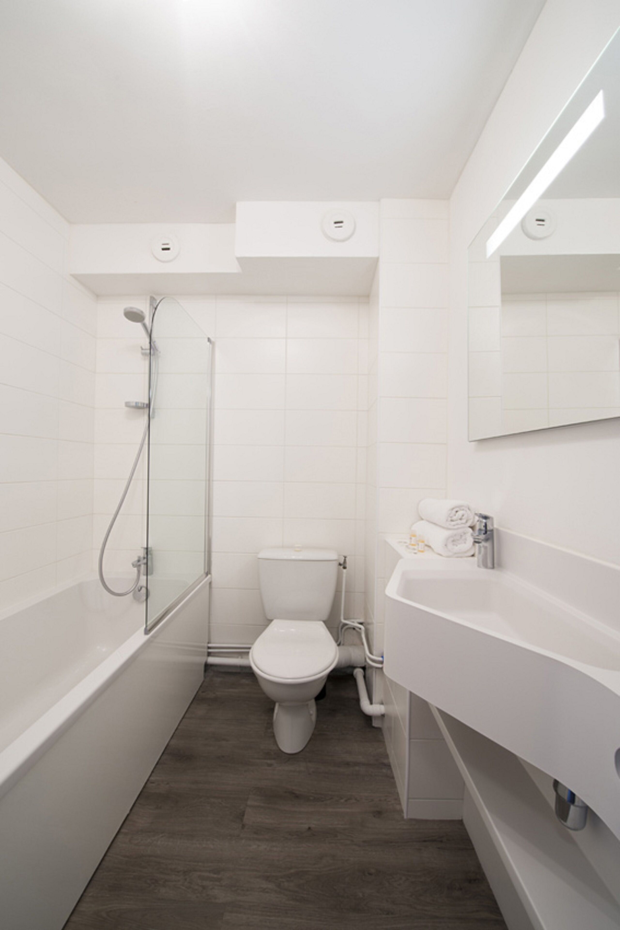 Une salle de bain moderne avec une douche à parois de verre, des toilettes blanches et un lavabo blanc avec un miroir au-dessus.