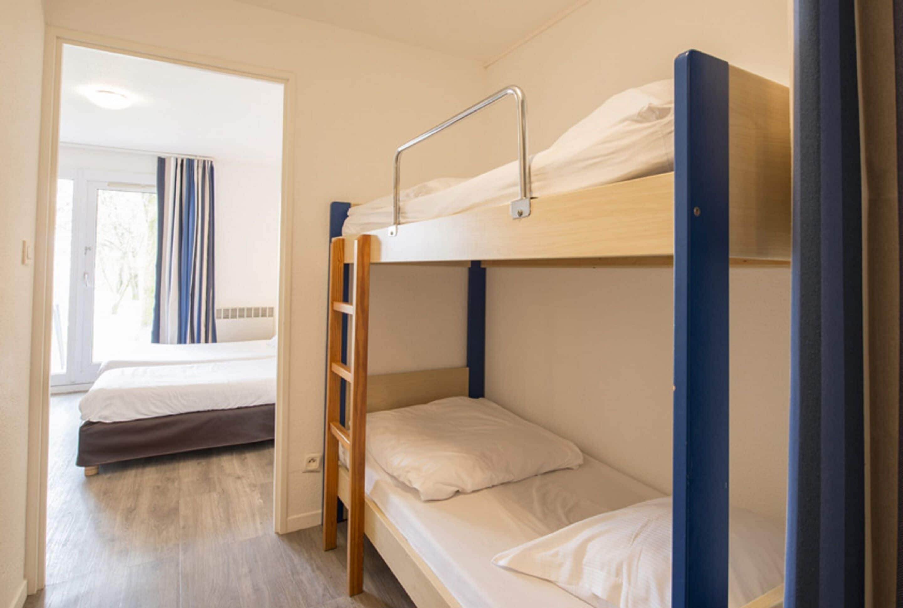 Una camera con un letto a castello, una scala, una finestra con tende e una porta che dà su un'altra stanza.