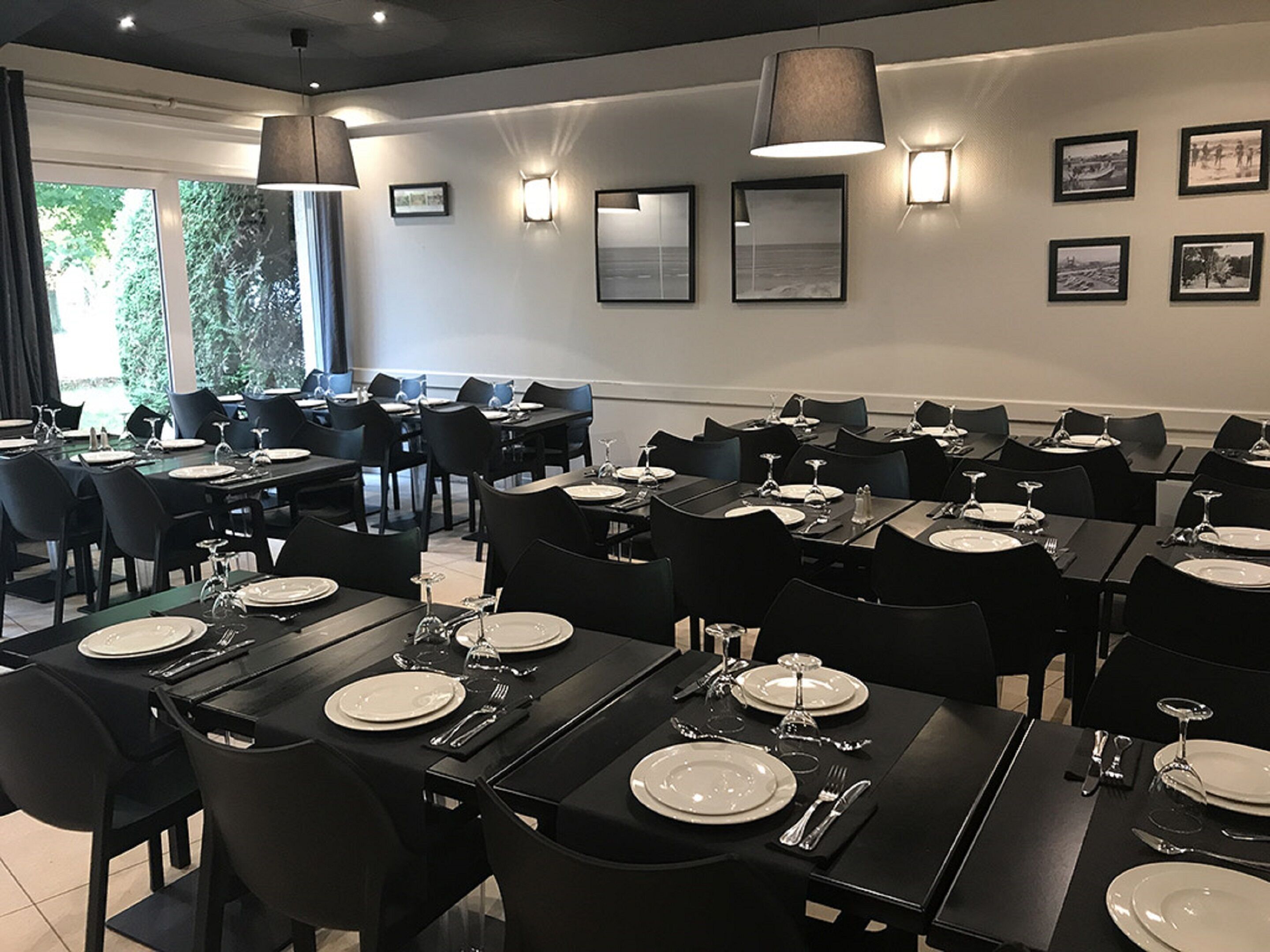 A dining area with multiple tables set for meals, black chairs, and wall-mounted lights.