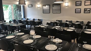 A dining area with multiple tables set for meals, black chairs, and wall-mounted lights.