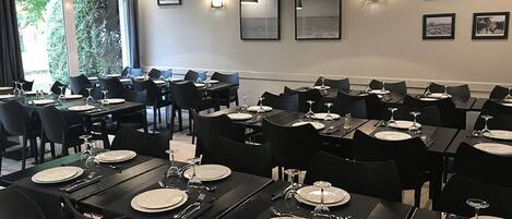 A dining area with multiple tables set for meals, black chairs, and wall-mounted lights.