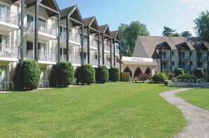 A hotel with multiple balconies, a well-maintained lawn, and a clear sky. - Hippotel (Le Touquet-Paris-Plage)