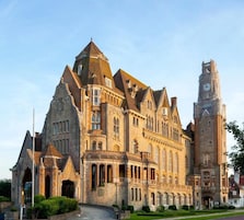 Un edificio grande e histórico, con una torre del reloj destacada y varios tejados a dos aguas.
