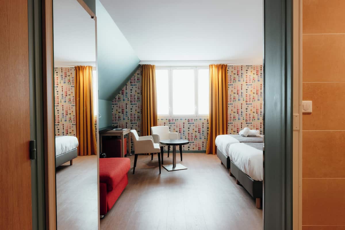 A hotel room with two beds, a desk, a chair, and a small table.