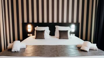 A neatly made bed with white linens and two pillows, a gray throw blanket, and two white towels on a dark wooden bed frame.