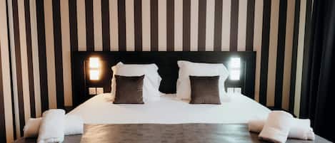 A neatly made bed with white linens and two pillows, a gray throw blanket, and two white towels on a dark wooden bed frame.