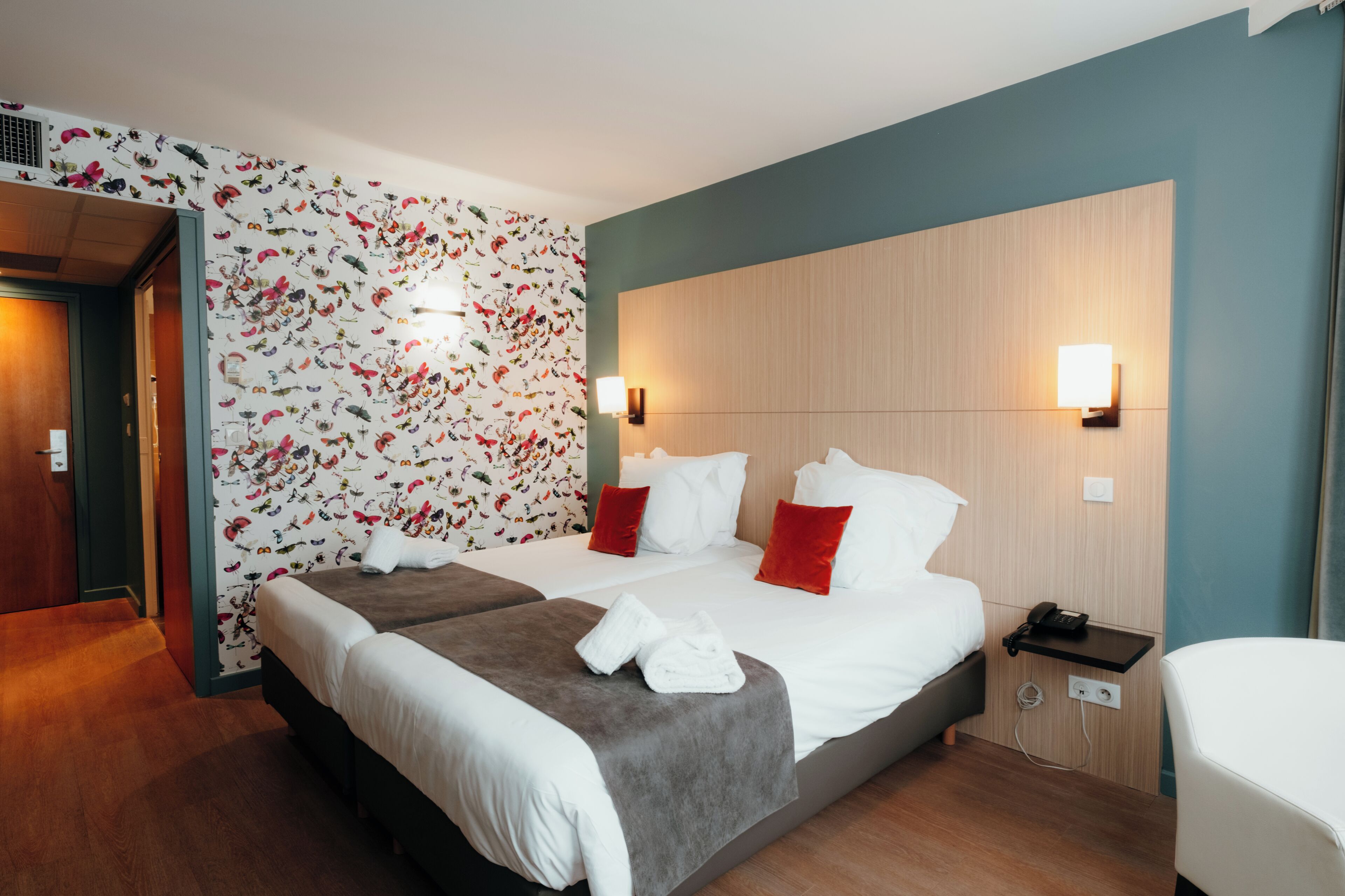Habitación de hotel con una cama grande, dos mesitas de noche, un teléfono en la pared y una puerta que da a otra habitación.
