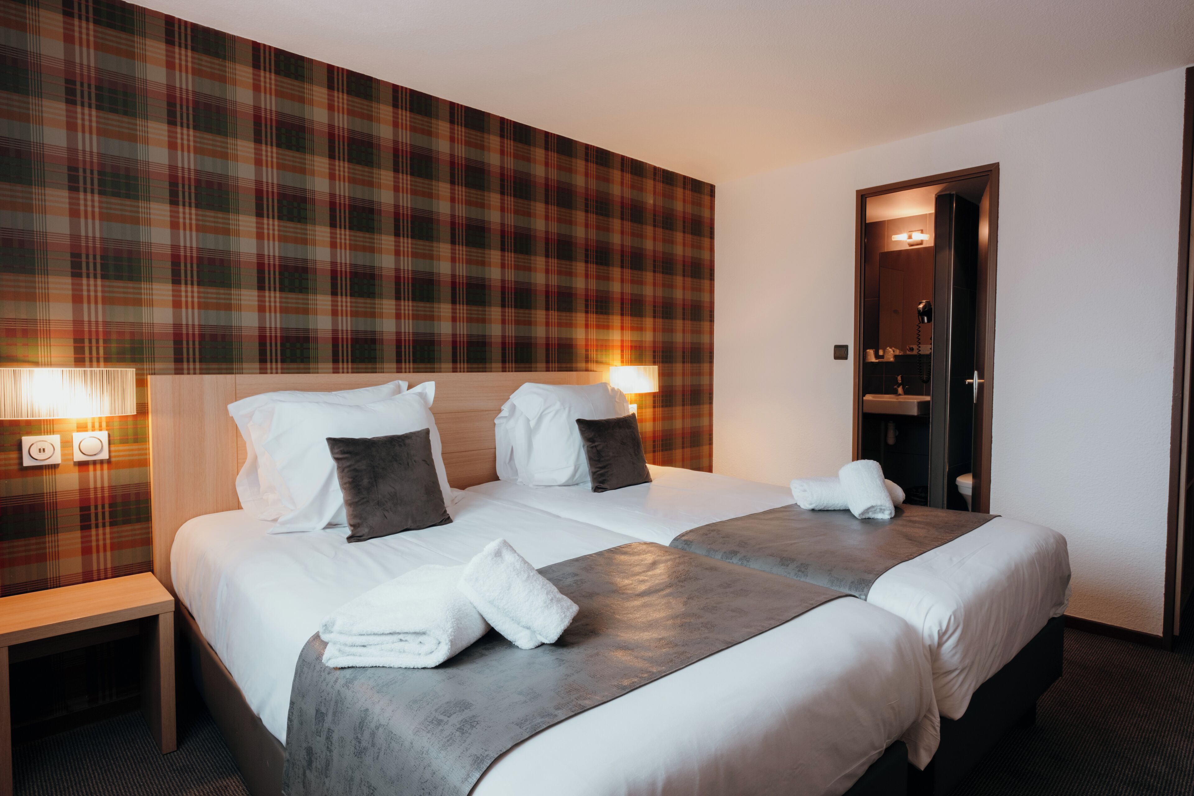 A hotel room with two beds, plaid wallpaper, bedside lamps, and a mirror.
