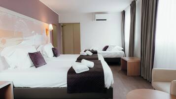 Une chambre d’hôtel avec trois lits, un canapé, une table ronde et un climatiseur fixé au mur.
