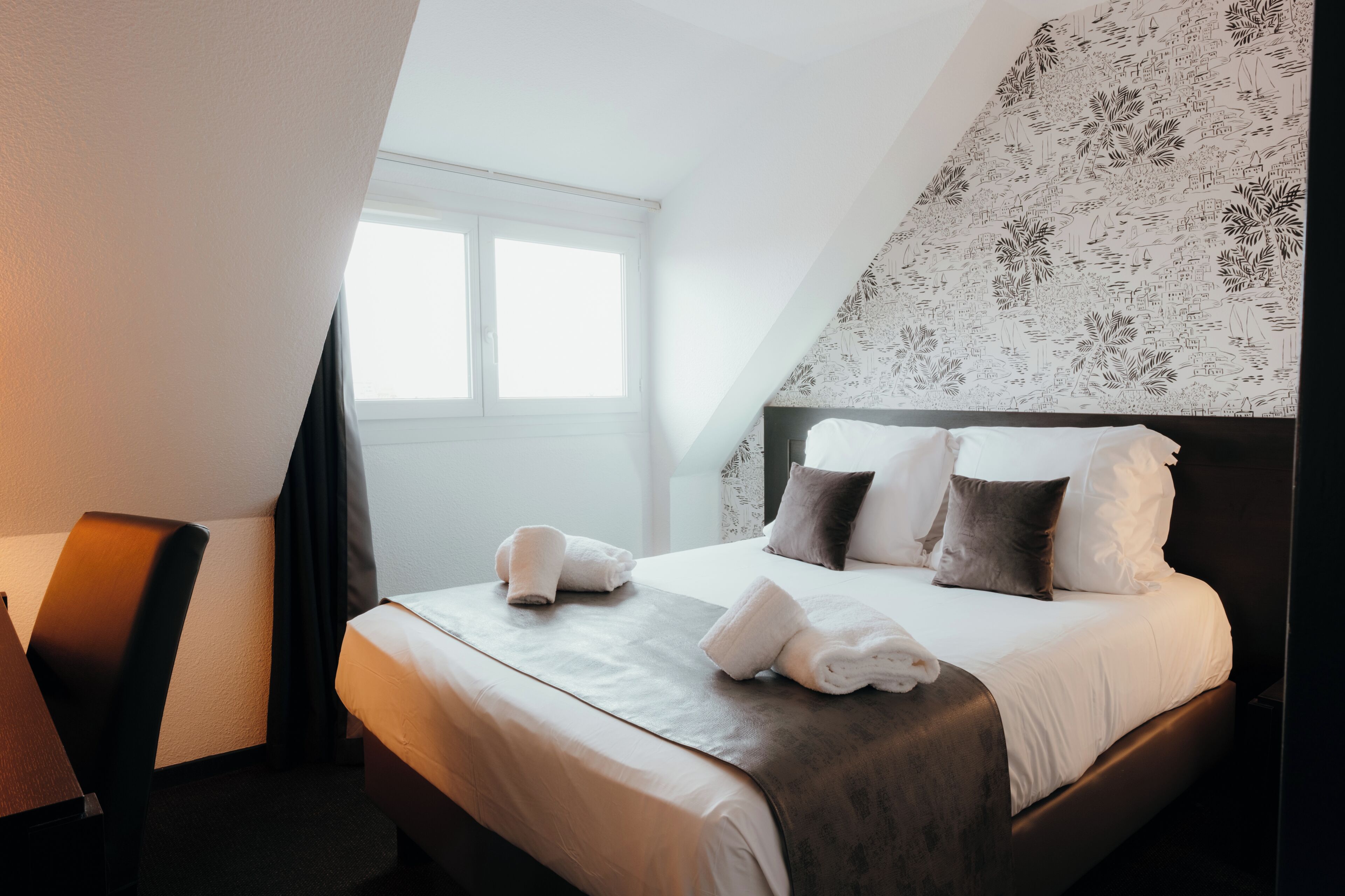 A hotel room with a neatly made bed, a chair, and a large window.