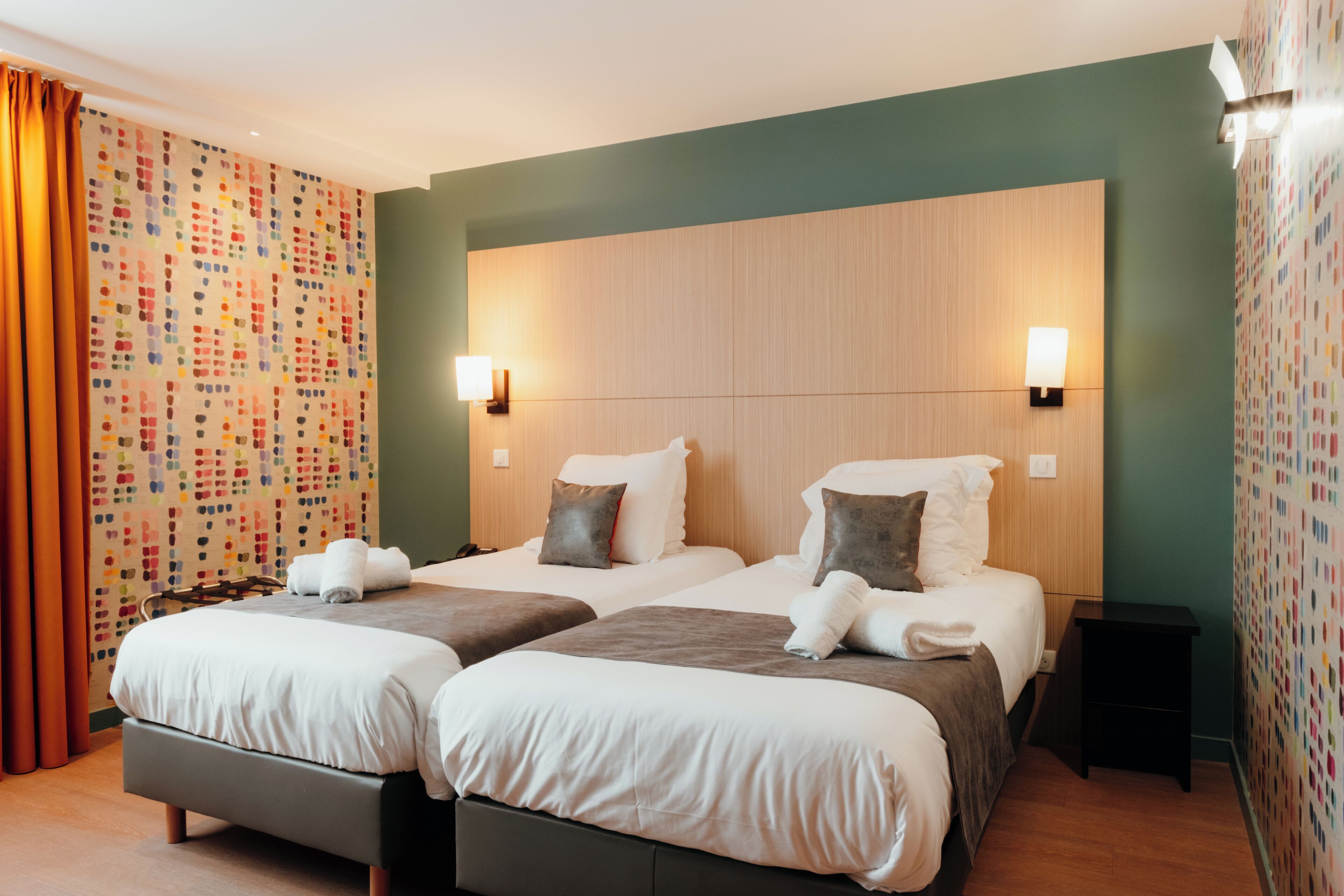 Habitació d'hotel amb dos llits, un capçal de llit de fusta i un disseny colorit a la paret.