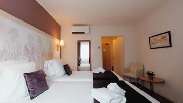 Habitación de hotel con dos camas, una mesita con una planta, una silla y una pared con un cuadro enmarcado.