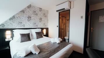 Une chambre d’hôtel avec un grand lit, une tête de lit ornée d’un motif floral, une table de chevet avec une lampe et un appareil de climatisation.