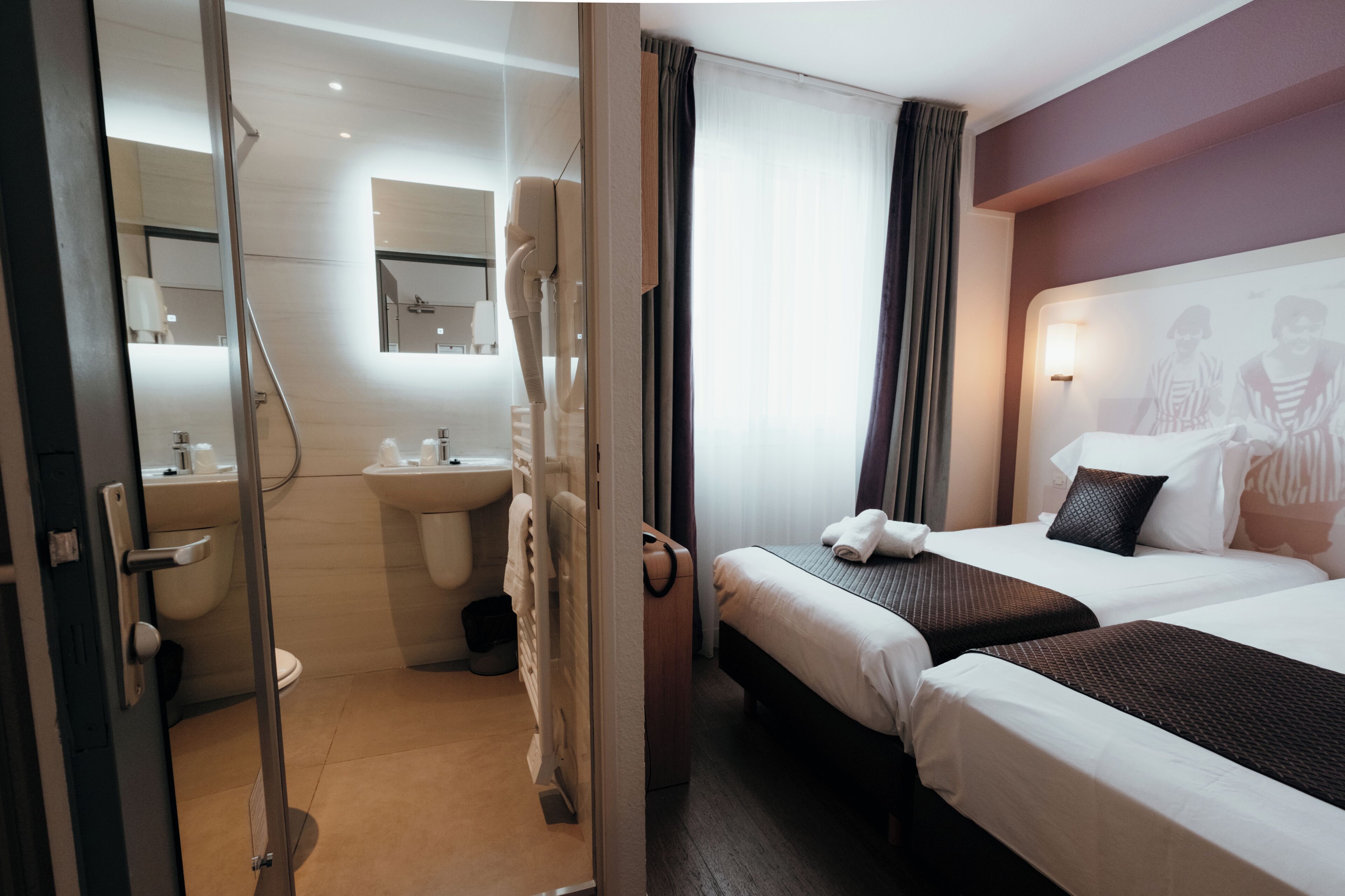 Ein Hotelzimmer mit Duschkabine aus Glas, einem Bett mit braunem Kopfteil und einem großen Spiegel über dem Waschbecken.