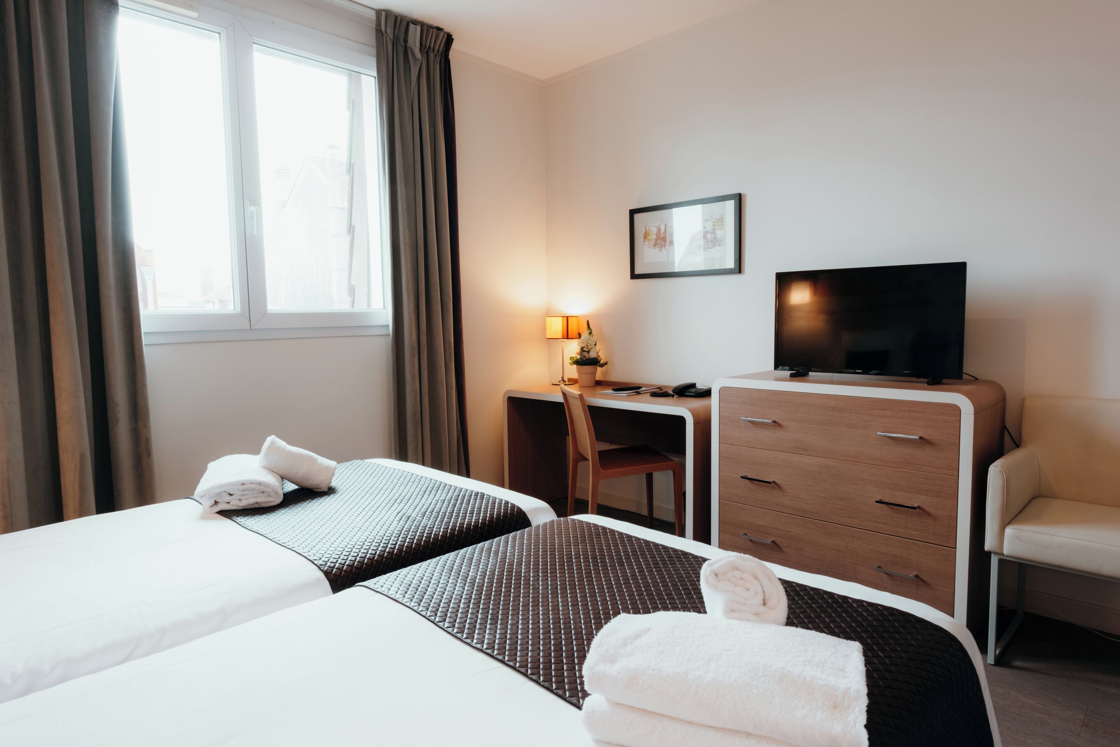 Une chambre d’hôtel avec deux lits, un bureau, une télévision et une chaise.