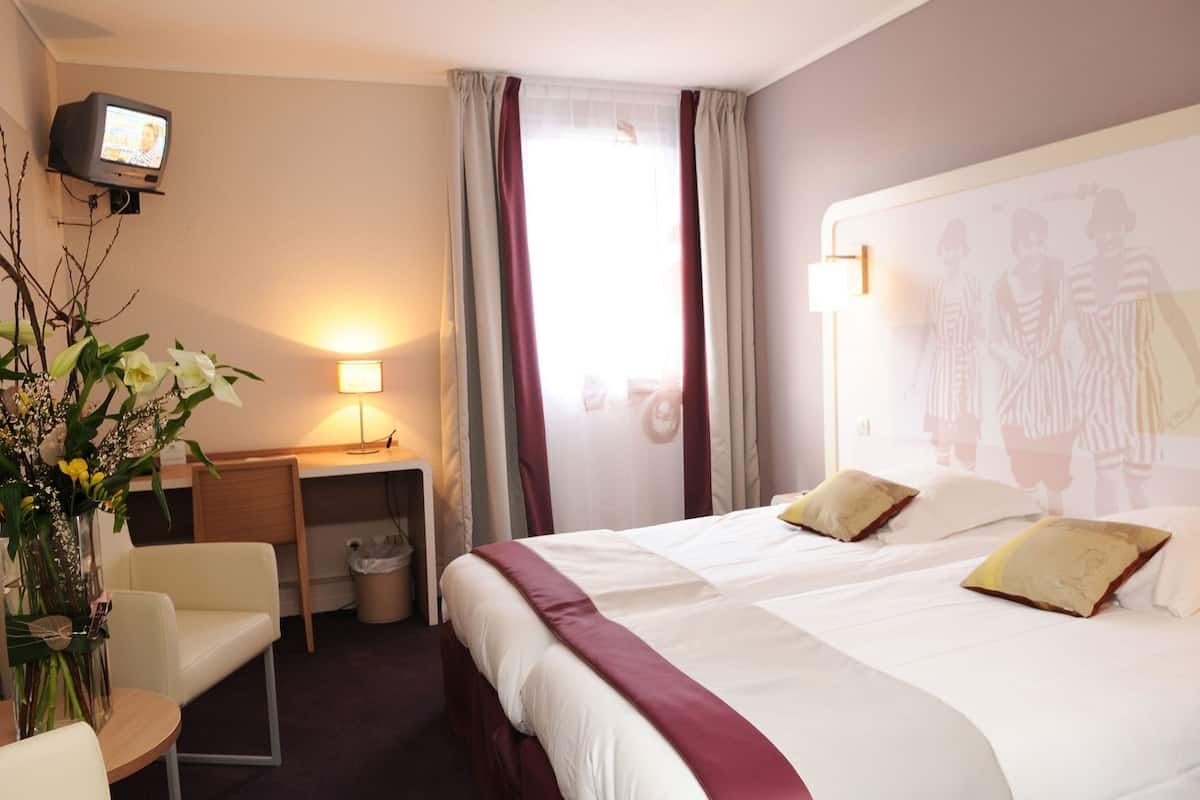 A hotel room with a bed, a desk, a chair, a TV, and a window with curtains.