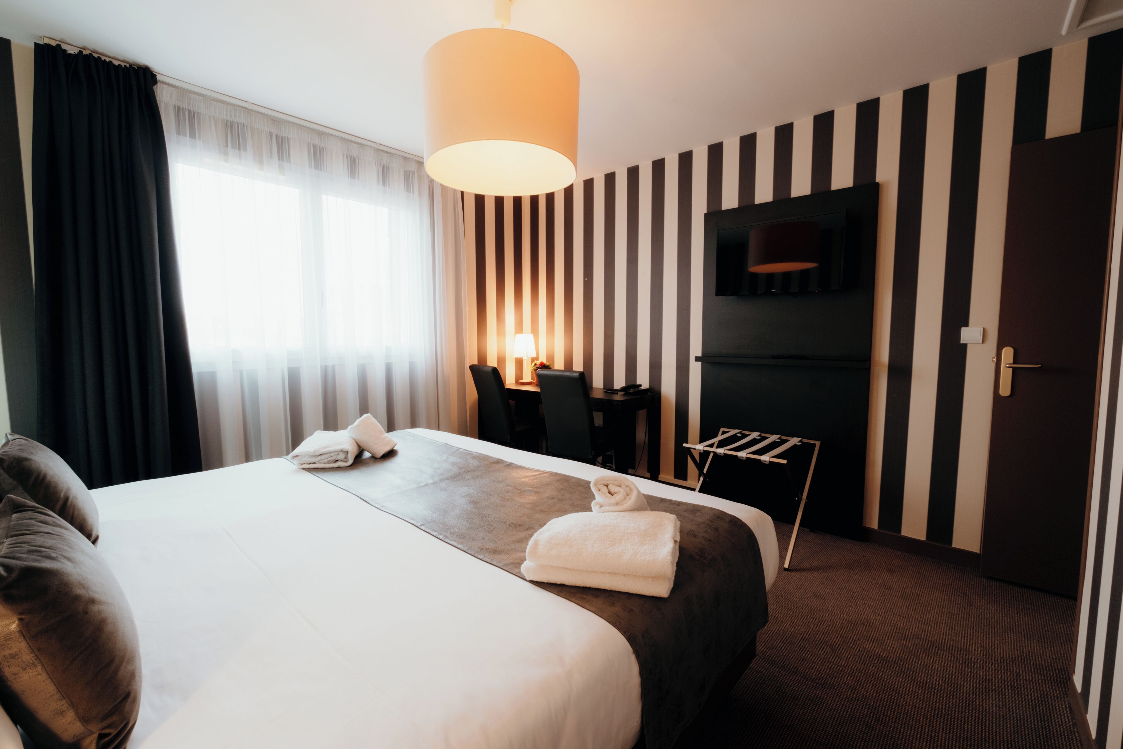 Habitación de hotel con una cama grande, un escritorio con silla, televisión y una puerta.