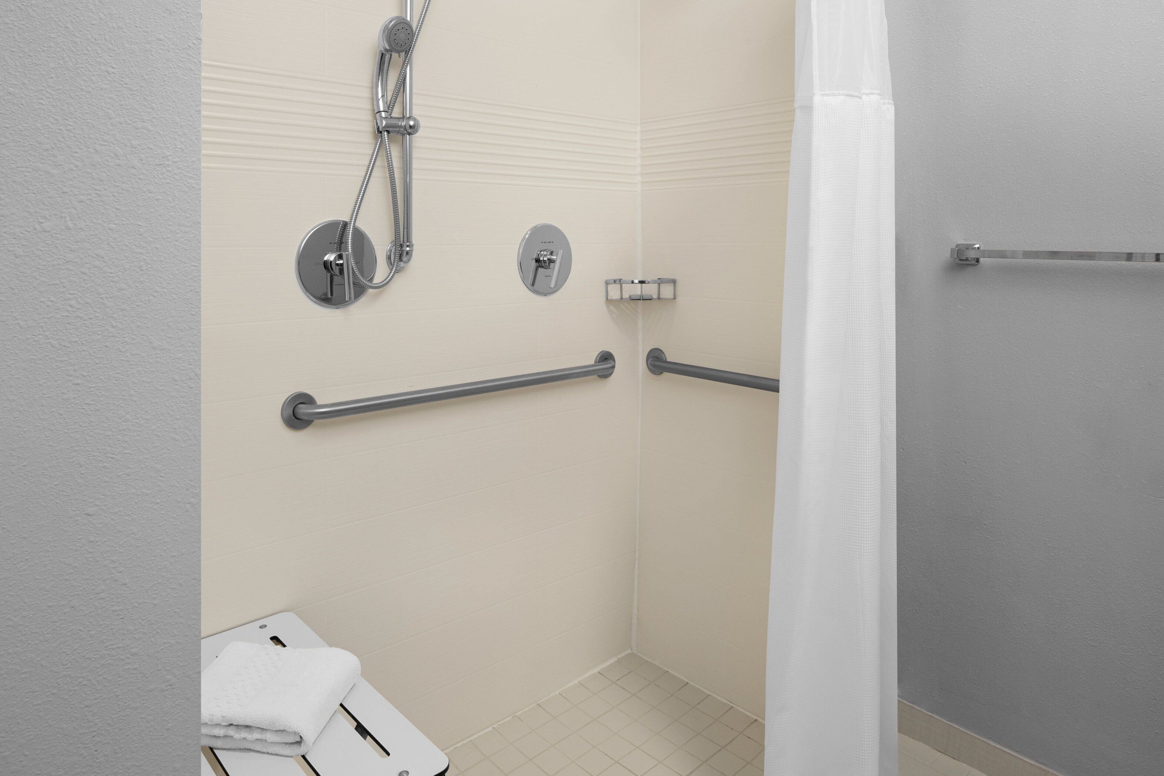A bathroom with a shower, grab bars, a towel rack, and a toilet.