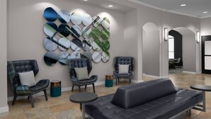 Un vestíbulo moderno con un sofá negro, dos sillones, una mesa redonda y una pared decorada con espejos circulares.