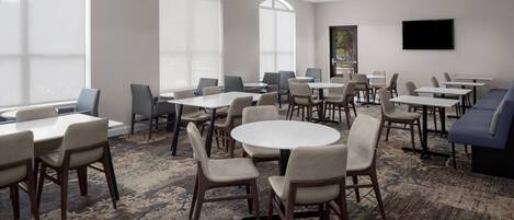 A conference room with round and rectangular tables, chairs, a sofa, and a TV on the wall.