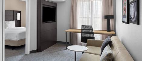A hotel room with a bed, a desk, a chair, and a sofa.