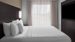 Habitación de hotel con una cama grande, televisión, ventana con cortinas y cabecero.