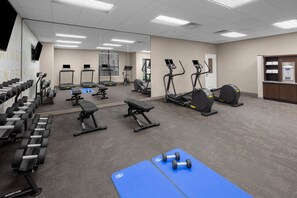 Un gimnasio con cintas de correr, elípticas, mancuernas y colchonetas de ejercicio.