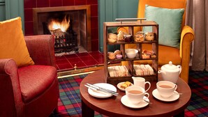 A cozy room with a fireplace, a red armchair, a yellow armchair, a small table with tea and pastries, and a bookshelf with snacks. - Loch Rannoch Hotel and Spa (Pitlochry)