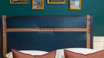 Ein Bett mit dunkelblauer Kopfteil, weißer Bettwäsche und zwei braunen Kissen. Vier gerahmte Bilder hängen an der Wand über dem Bett.