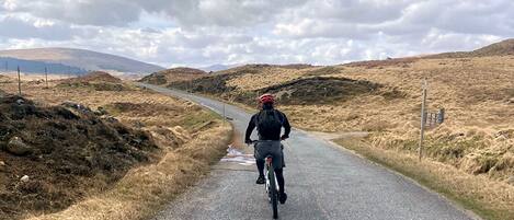 A cyclist on a gravel road with dry grass on either side and a cloudy sky.