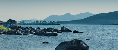 A calm lake with large rocks in the foreground and mountains in the background.