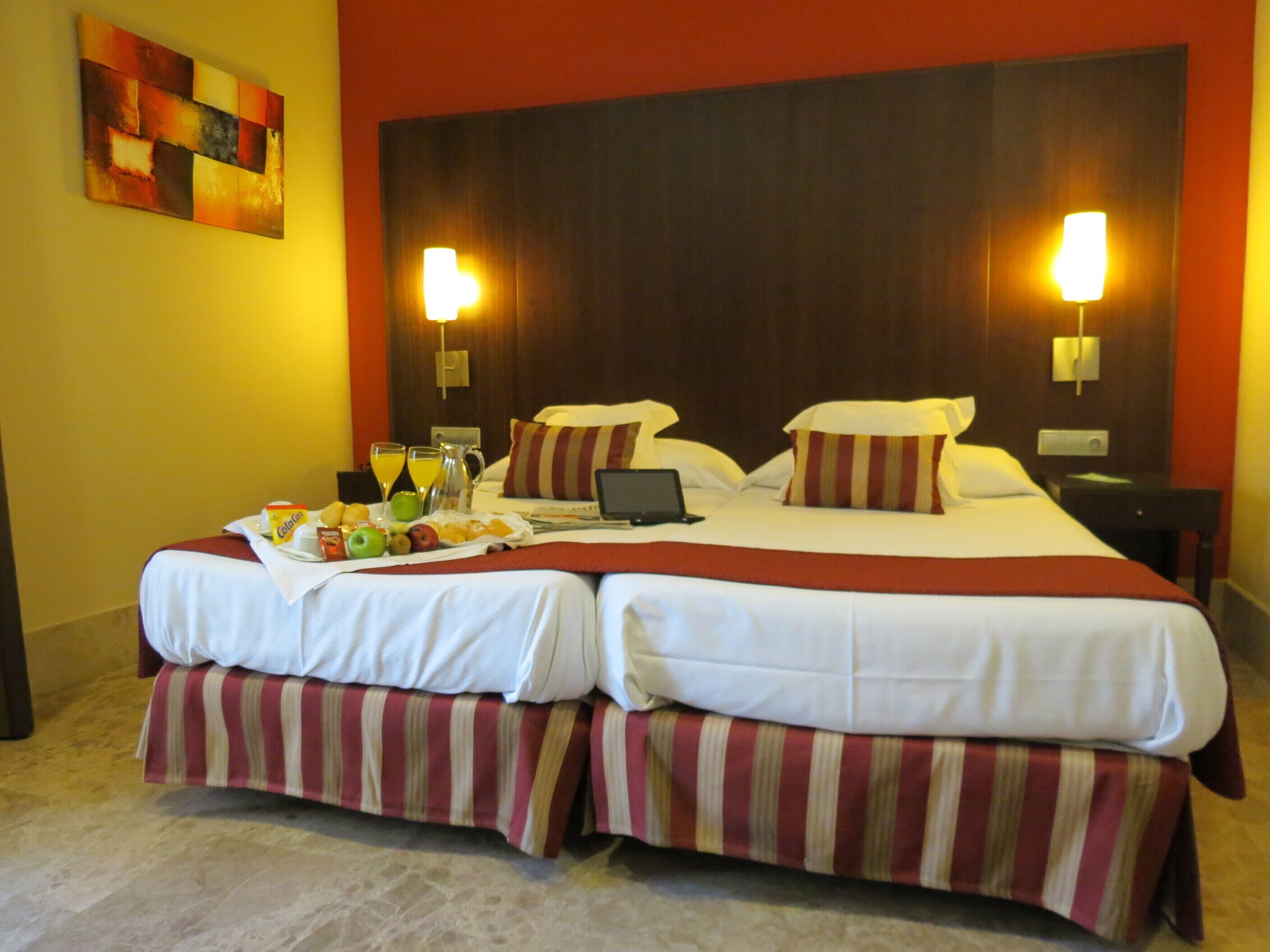 A double bed with a red and white striped bed skirt, a laptop on the bed, and a breakfast tray with fruits and juice.
