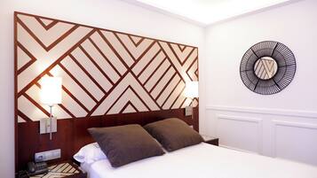 Habitación de hotel con cama, dos almohadas, mesita de noche con teléfono y pared decorada con un diseño geométrico y un motivo circular.