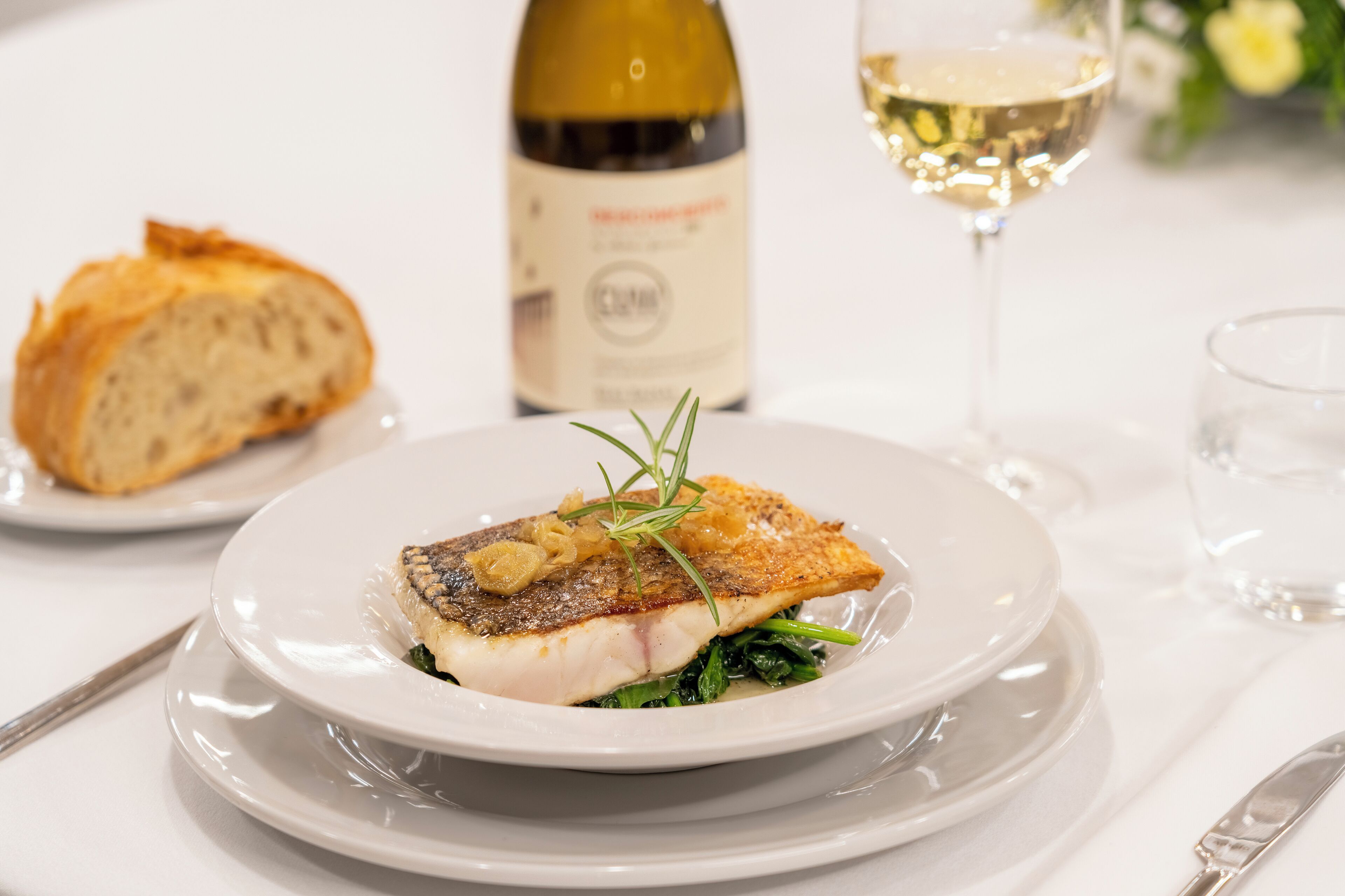 Ein Teller mit einem Fischfilet, einer Weinflasche und einem Weinglas auf einem Tisch.