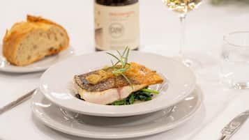 A plate of food with a fish fillet, a bottle of wine, and a glass of white wine on a table.