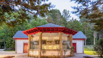 Un pequeño edificio con techo rojo, entrada cubierta y puerta de cristal, rodeado de árboles.
