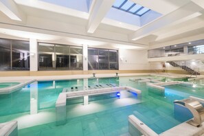 Una amplia piscina cubierta con múltiples carriles, techo de cristal y una escalera que sube a un nivel superior.