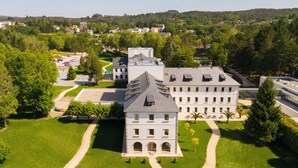 Un grand immeuble à étages, doté d’une façade symétrique, entouré de pelouses bien entretenues et de quelques arbres.